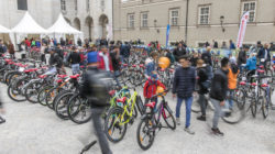 Eine Menschenmenge, die zwischen Reihen von Fahrrädern spaziert, die im Freien in der Nähe von weißen Zelten und historischen Gebäuden ausgestellt sind.