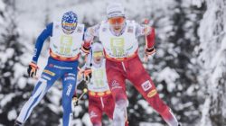 Drei Skilangläufer, darunter Mario Seidl, rasen in nummerierten Startnummern und bunten Anzügen durch einen verschneiten Wald.