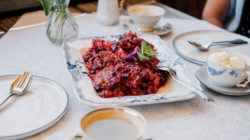 Ein Teller mit Beerendessert mit Minze, serviert mit Kaffeebechern und Eis auf einer weißen Tischdecke.
