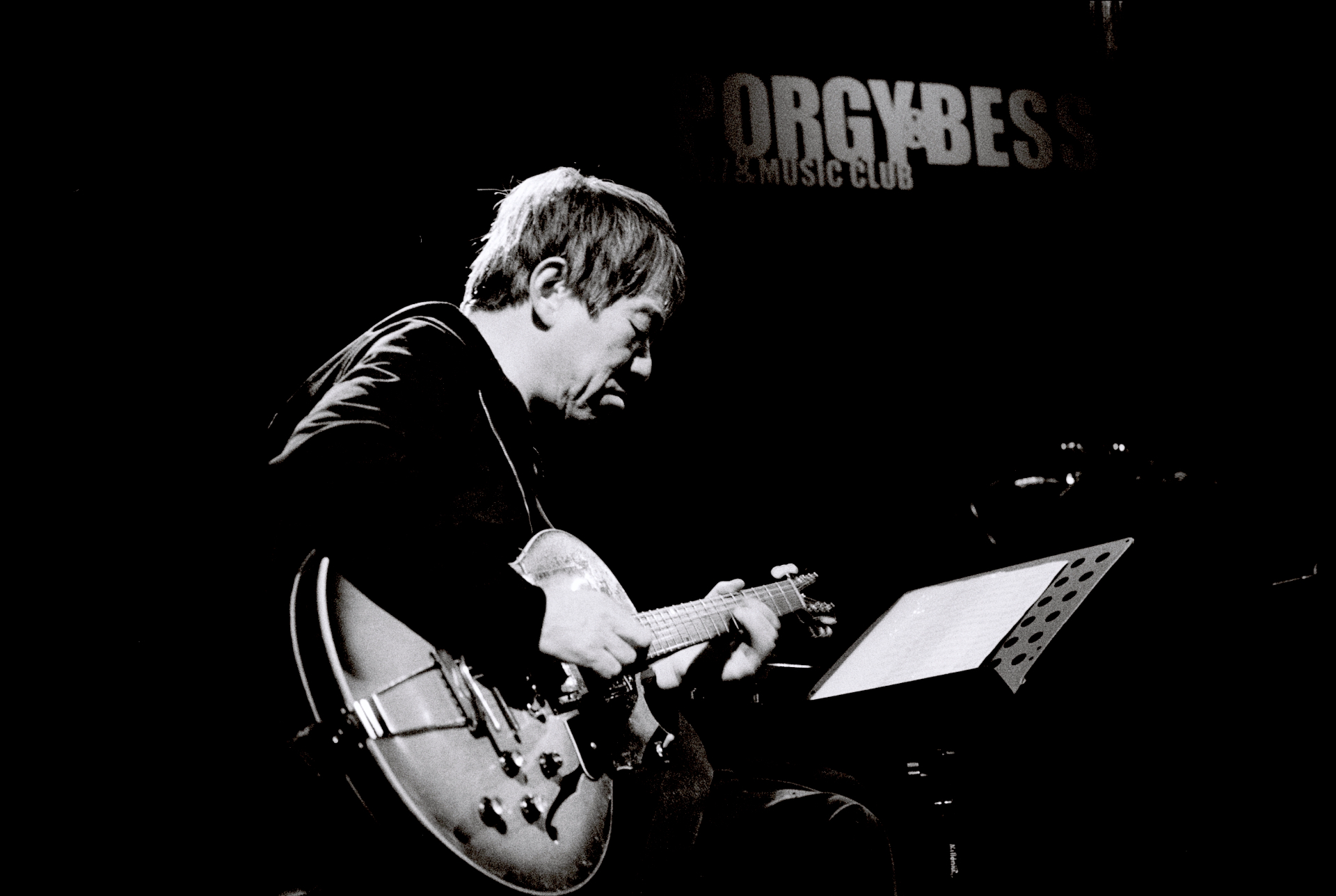 Ein Musiker spielt E-Gitarre auf der Bühne eines Veranstaltungsortes mit einem Porgy & Bess Music Club-Schild im Hintergrund.