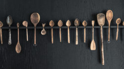 Eine Reihe von verschiedenen Holzlöffeln und -utensilien hängt an einem dunklen Wandregal.