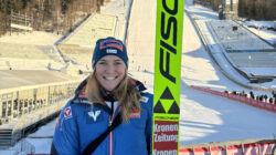 Frau in Wintersportkleidung, lächelnd, mit einem Ski in der Hand - Sara Marita Kramer gehört zu den besten Skispringerinnen der Welt.