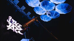 Bühne mit 3 Tage Jazz-Schild, Mikrofonen und blau beleuchteten Schirmen, die von der Decke hängen.