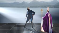 Ein Wolf-das Mystische Mann in einem Anzug mit Teufelshörnern steht einem Bischof an einem österreichischen Bergsee gegenüber.