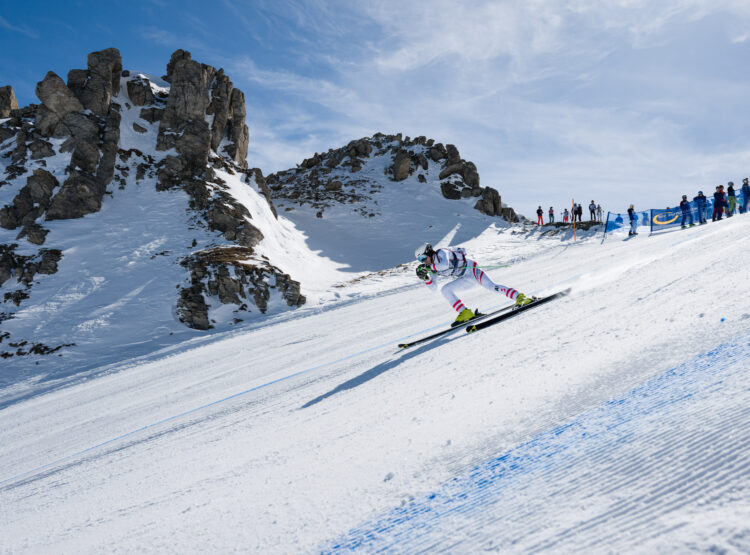 Ein Skifahrer rast in Die Nord den Hang hinunter, umrahmt von felsigen Bergen und jubelnden Zuschauern im Hintergrund.