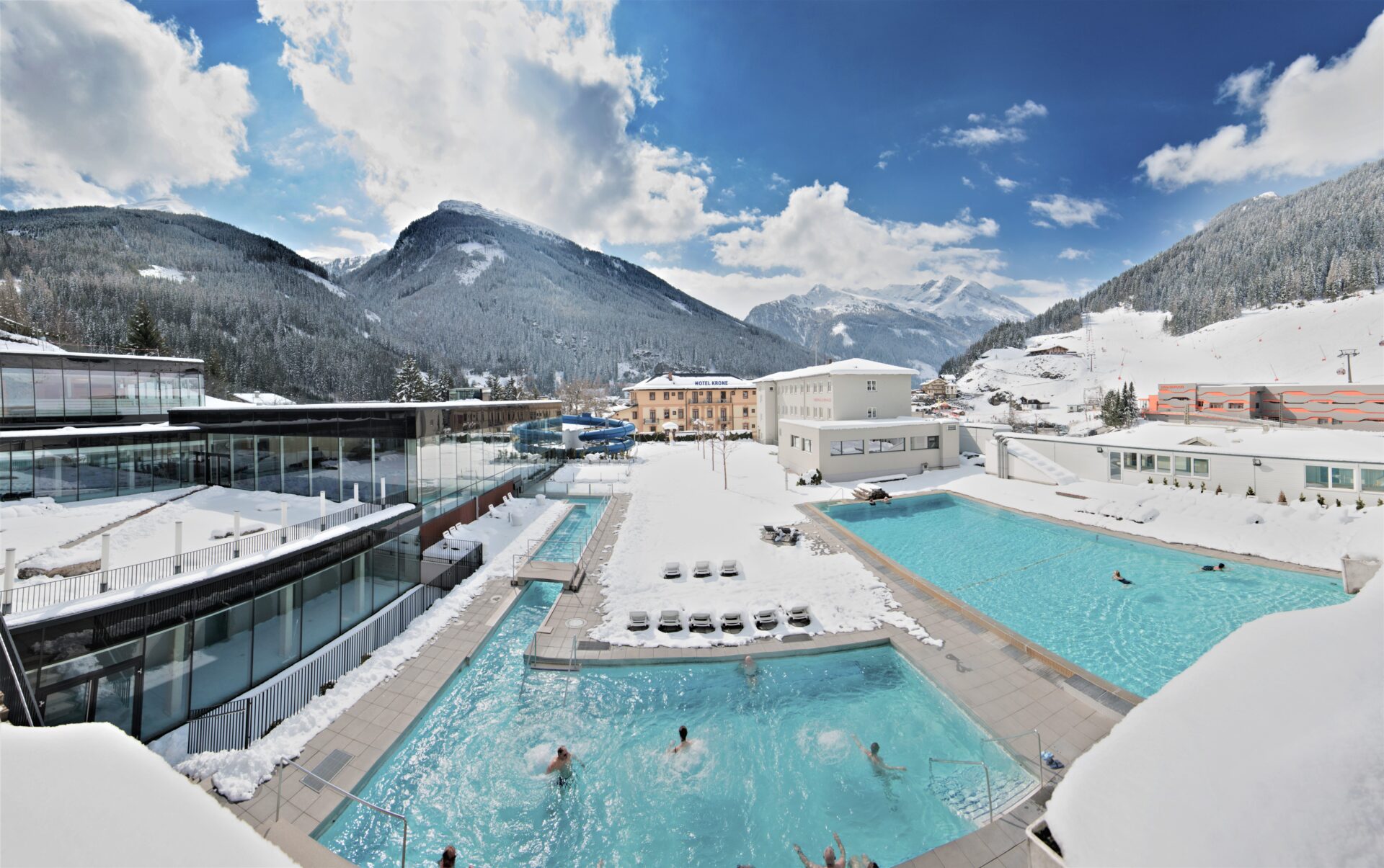 Thermalbäder im Freien, in denen Menschen schwimmen, verschneite Berge, moderne Gebäude und Zugang zu Ski- und Thermentickets.