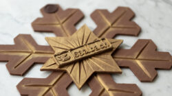 Eine Schokolade-Schneeflocke mit goldenen Highlights und einem lächelnden Logo auf einer Marmoroberfläche.