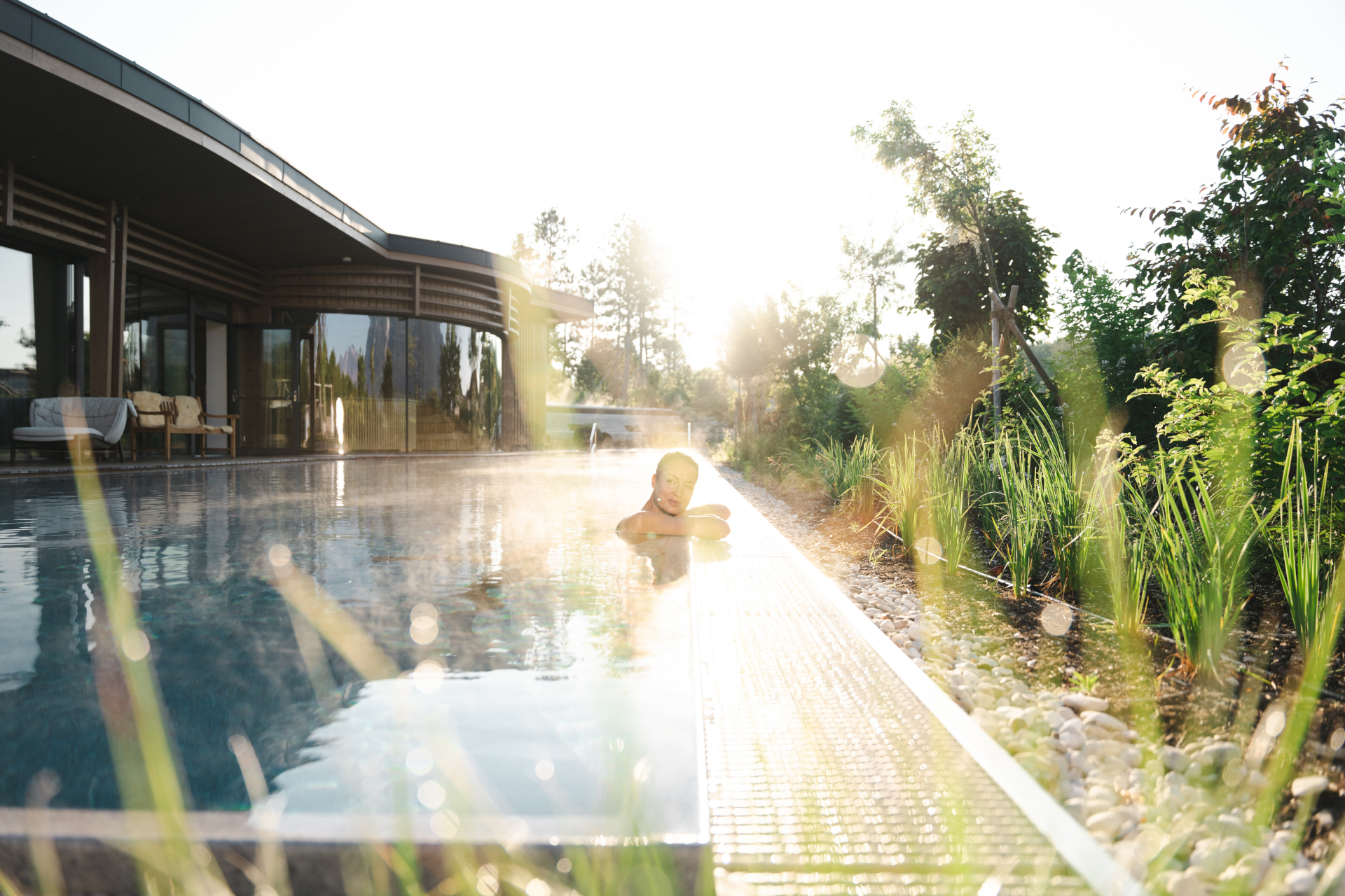 Entspannen Sie sich bei Sonnenaufgang im Au&szlig;enpool des Laschenskyhofs, der von Gr&uuml;nfl&auml;chen und einem modernen Geb&auml;ude umgeben ist.