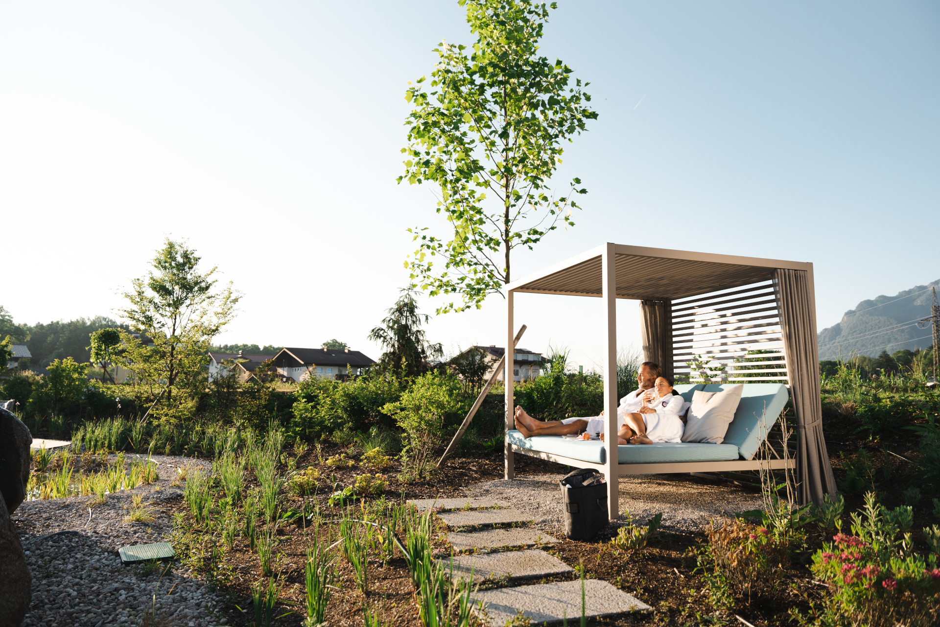 Eine Person, die sich auf einem Himmelbett im Freien auf dem Laschenskyhof entspannt, umgeben vom Gr&uuml;n des Gartens und unter einem klaren blauen Himmel.