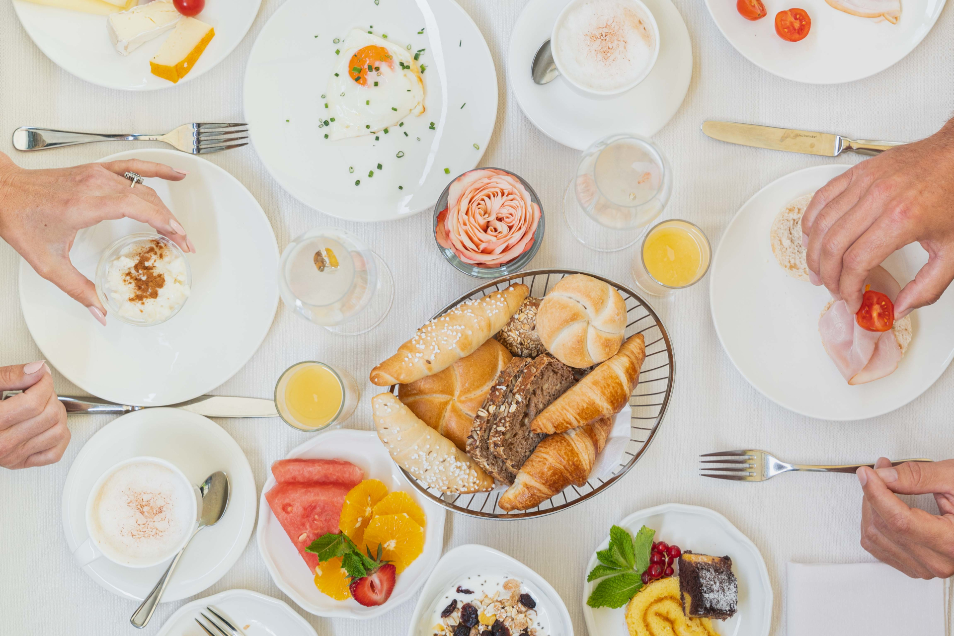 Frühstückstisch im Laschenskyhof mit Gebäck, Obst, Eiern, Kaffee und Menschen, die nach Essen auf weißen Tellern greifen.