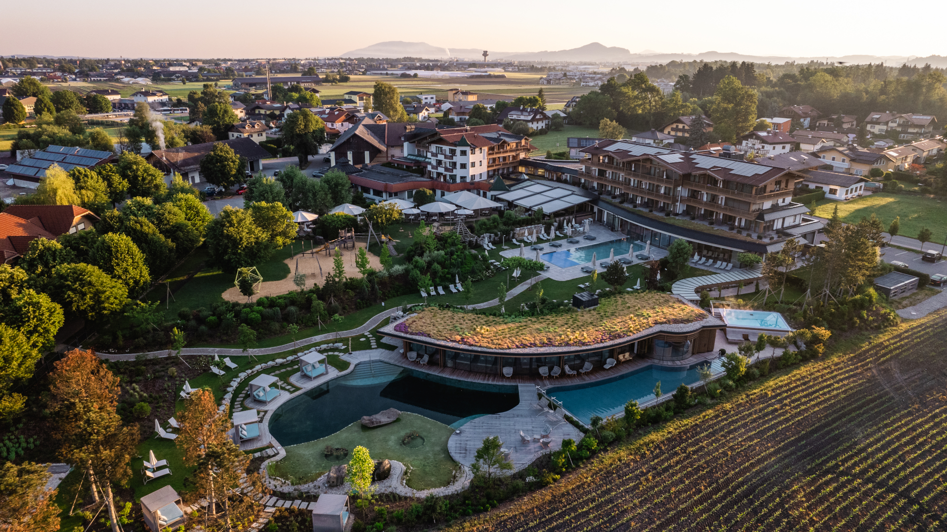 Luftaufnahme des Luxusresorts Laschenskyhof mit Pools, G&auml;rten und Loungebereichen inmitten von H&auml;usern und Feldern.