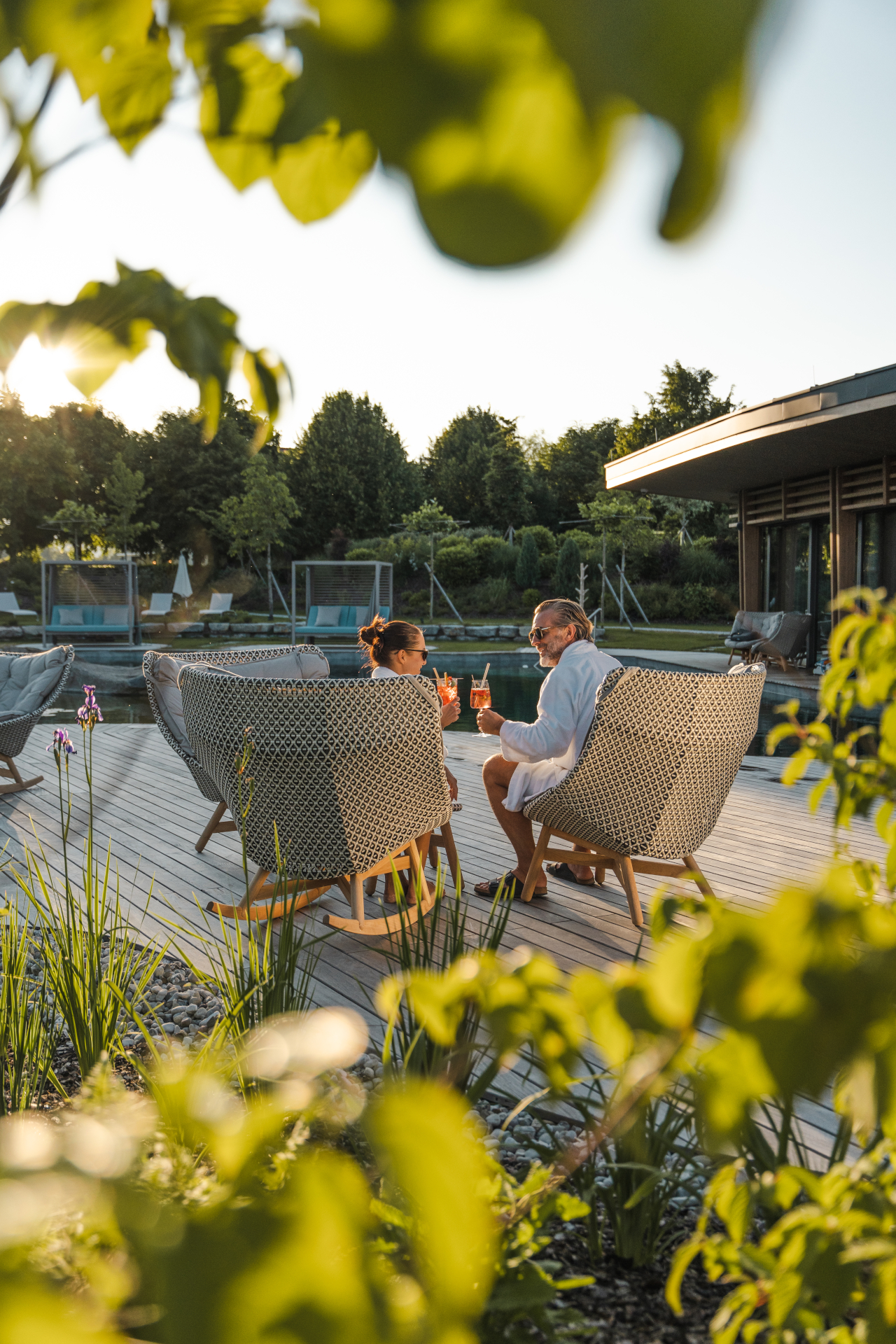 Zwei Personen sto&szlig;en an einem sonnigen Tag am Pool des Laschenskyhofs mitten im Gr&uuml;nen an.