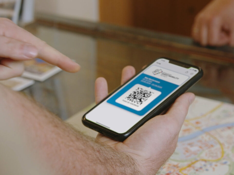 Eine Person hält ein Smartphone, auf dem ein QR-Code angezeigt wird, während eine andere Hand auf den Bildschirm zeigt.