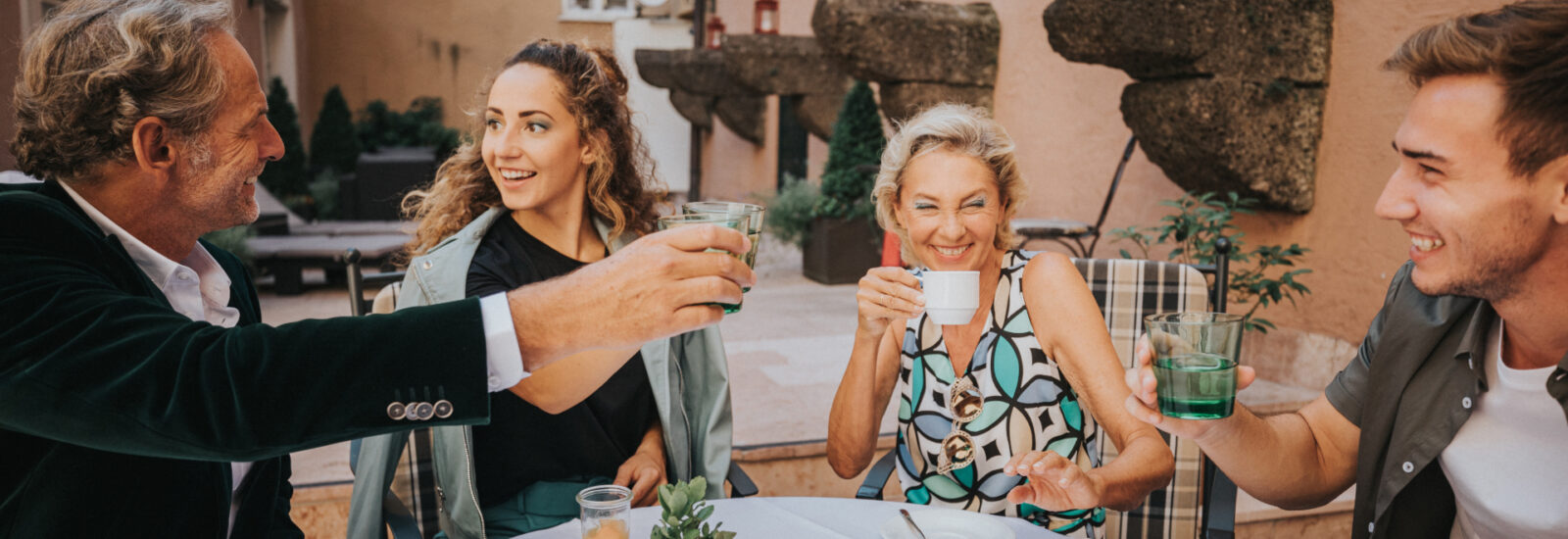 Vier Menschen lächeln und stoßen gemeinsam an einem Cafétisch im Freien an.