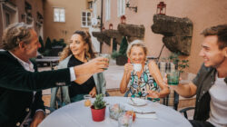 Vier Menschen lächeln und stoßen gemeinsam an einem Cafétisch im Freien an.