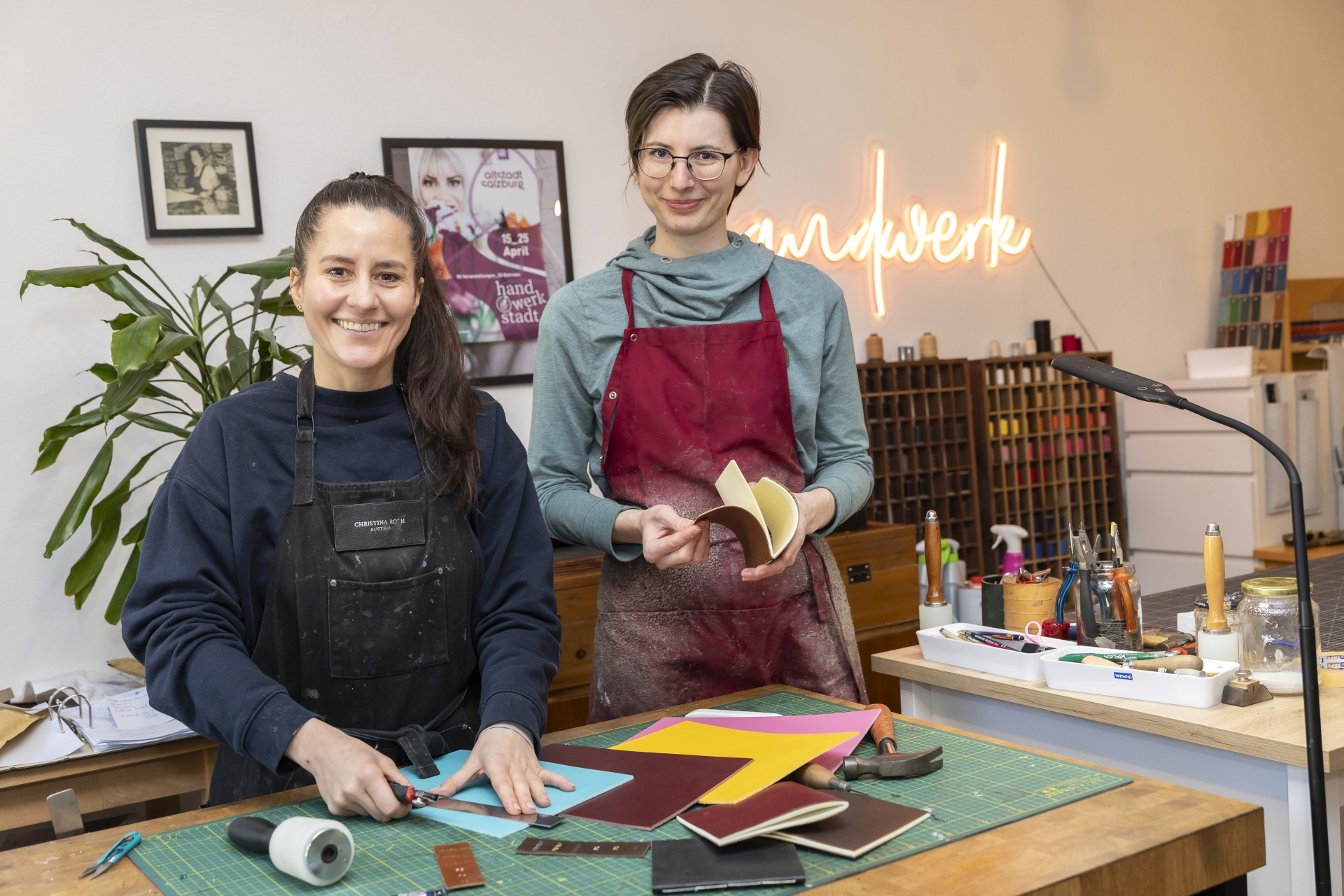 Zwei Frauen arbeiten mit bunten Materialien an einem Basteltisch, lächelnd in einer gut beleuchteten Werkstatt.