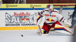 Ein Eishockeytorwart in weißer Kleidung blockiert einen Puck vor dem Netz während eines Red Bull Invitational-Spiels.