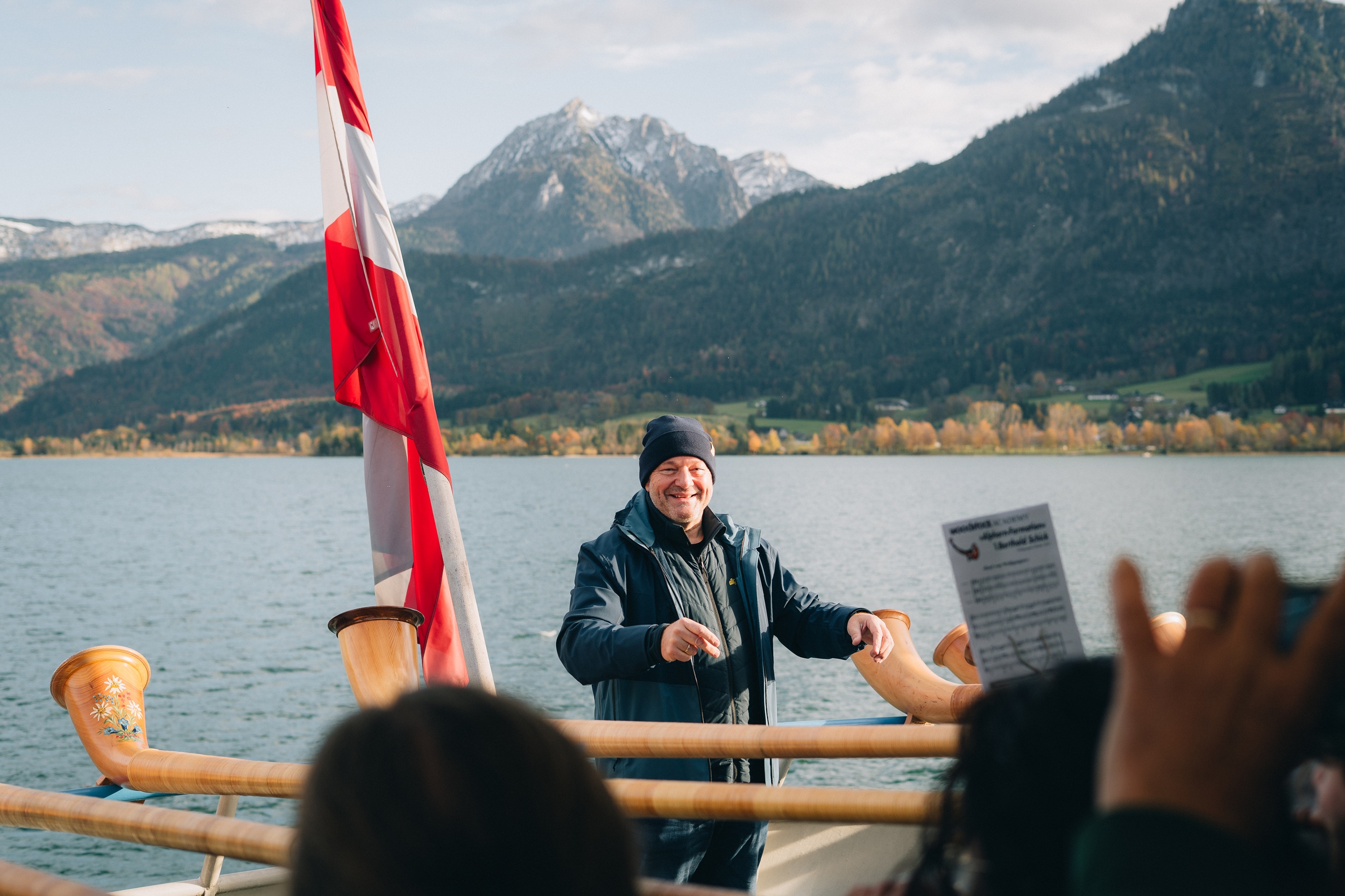 Ein Mann mit einer M&uuml;tze l&auml;chelt auf einem Boot in der N&auml;he einer rot-wei&szlig;en Flagge und tr&auml;gt seine Woodstock Academy-Ausr&uuml;stung.