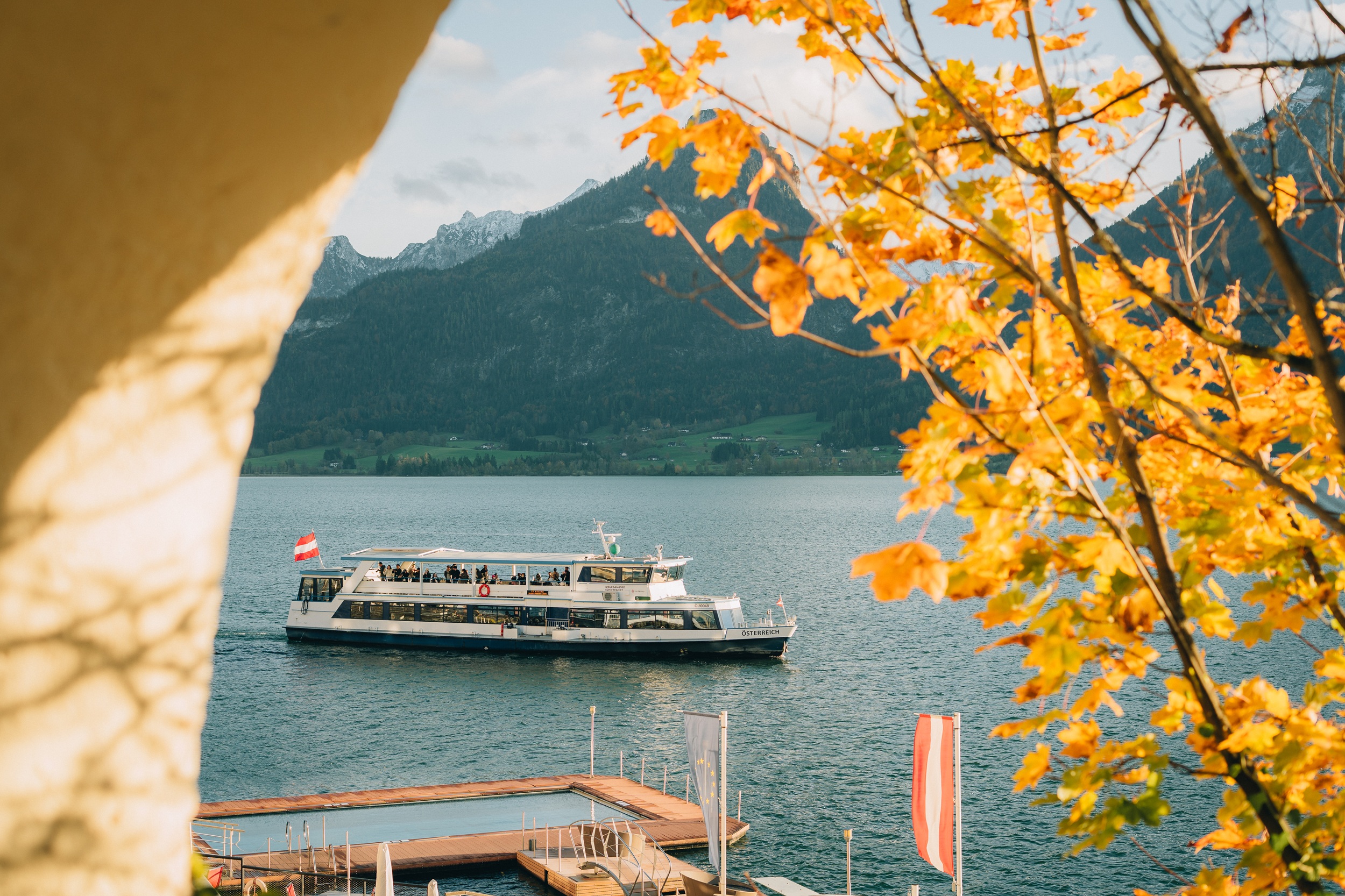 Ein Boot f&auml;hrt auf einem See in der N&auml;he der Woodstock Academy, mit Herbstbl&auml;ttern und Bergen im Hintergrund.