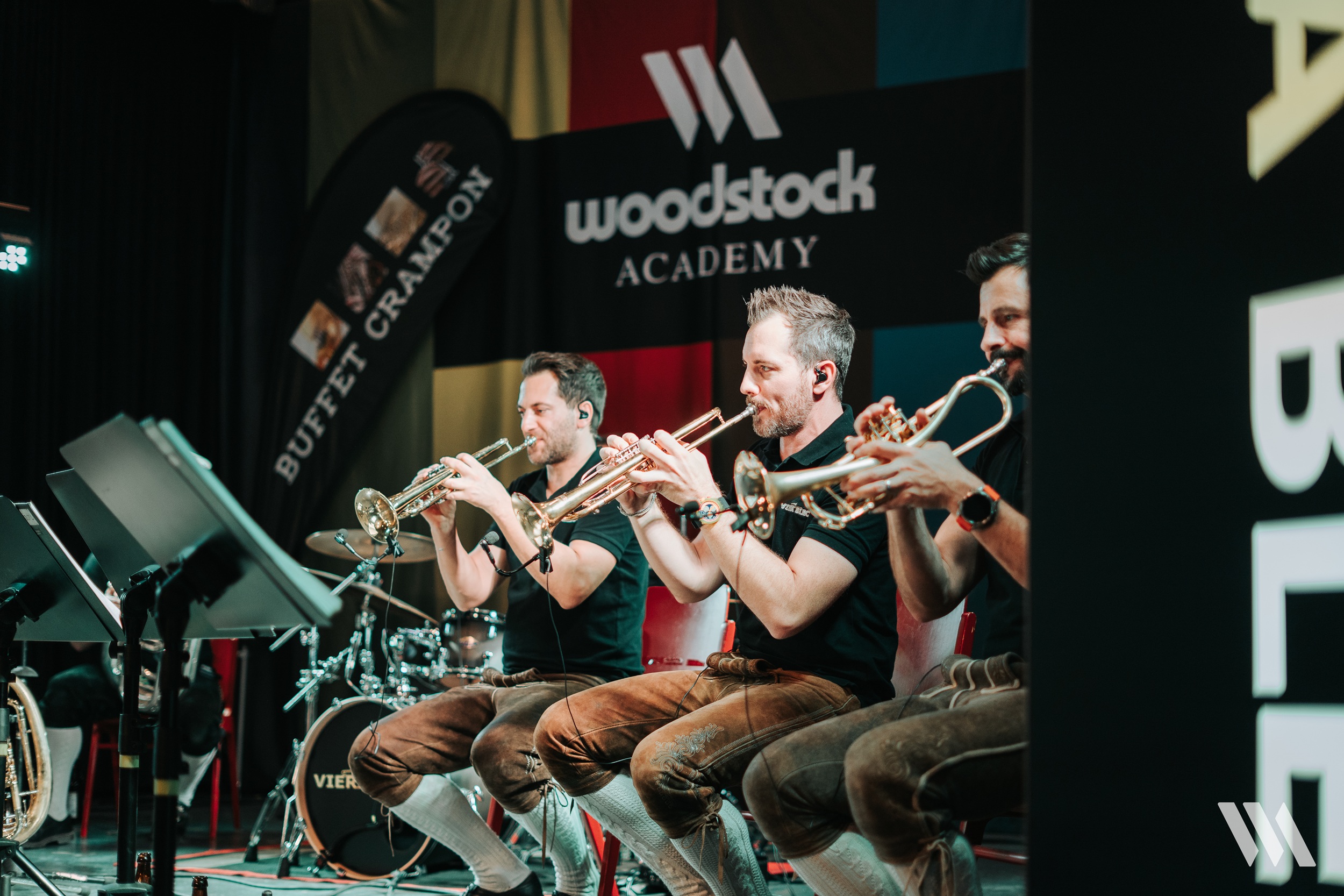 Drei M&auml;nner spielen auf Trompeten in der Woodstock Academy, mit Fahnen und Instrumenten im Hintergrund.