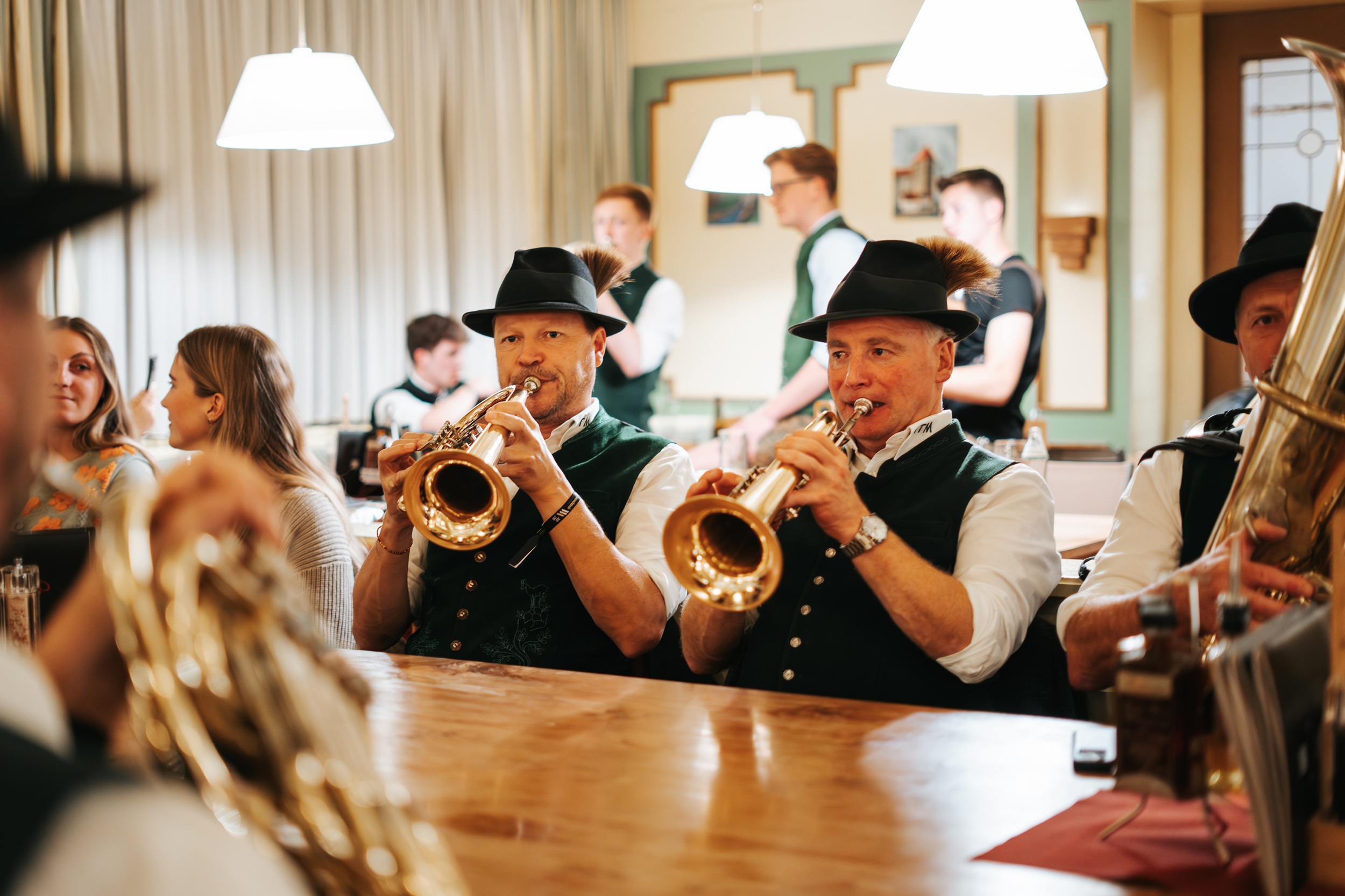 Zwei M&auml;nner in traditioneller Kleidung spielen bei einer lebhaften Versammlung in der Woodstock Academy Blasinstrumente.