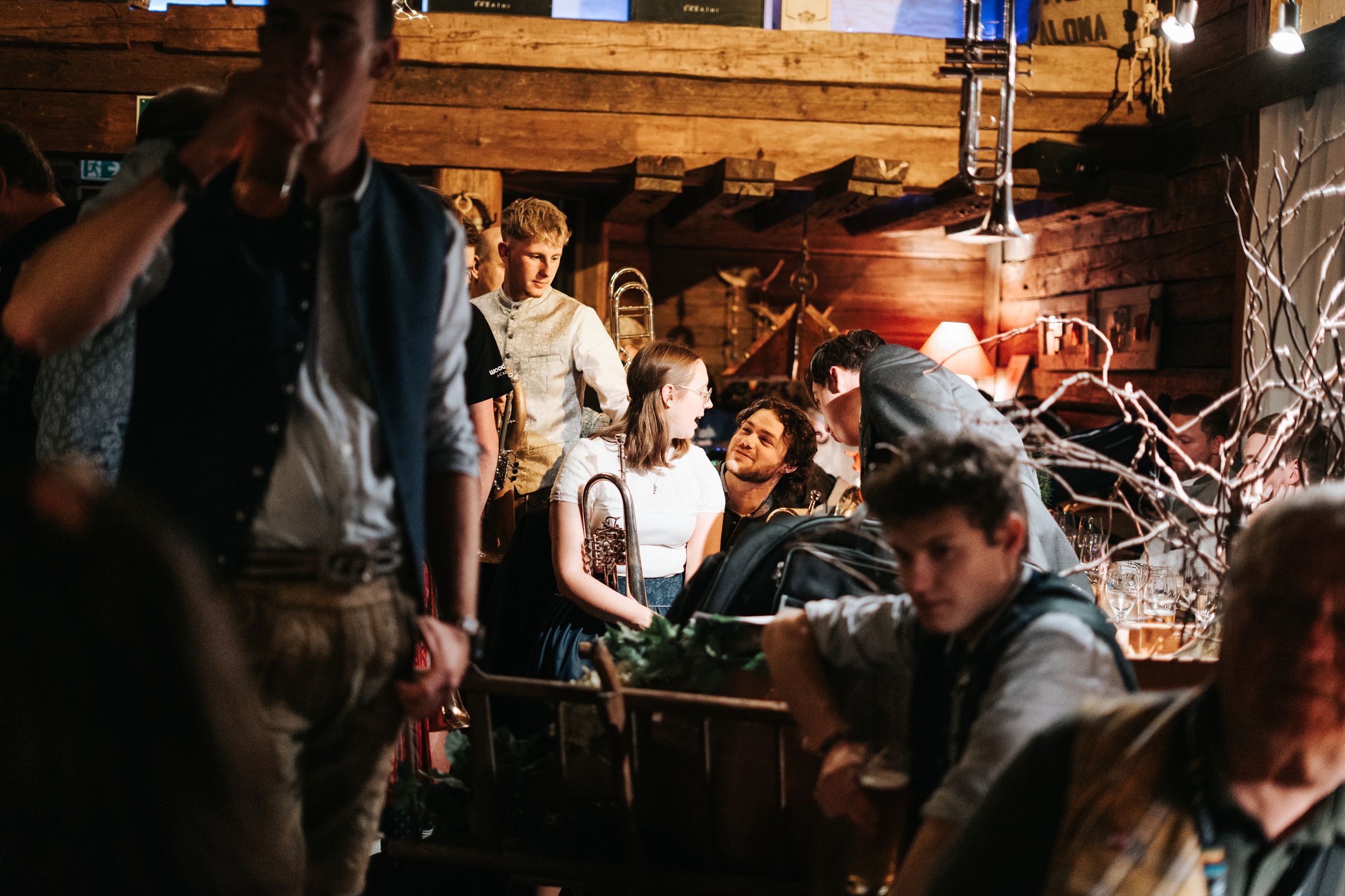 Eine Gruppe der Woodstock Academy in traditioneller Kleidung unterh&auml;lt sich in einem rustikalen, schwach beleuchteten Raum mit Instrumenten.