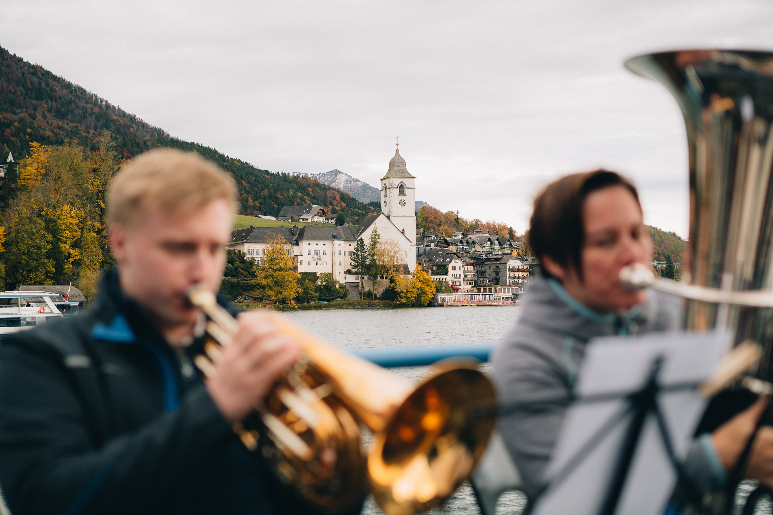 Zwei Personen spielen Blasinstrumente im Freien an der Woodstock Academy, mit einer Kirche und Bergen im Hintergrund.