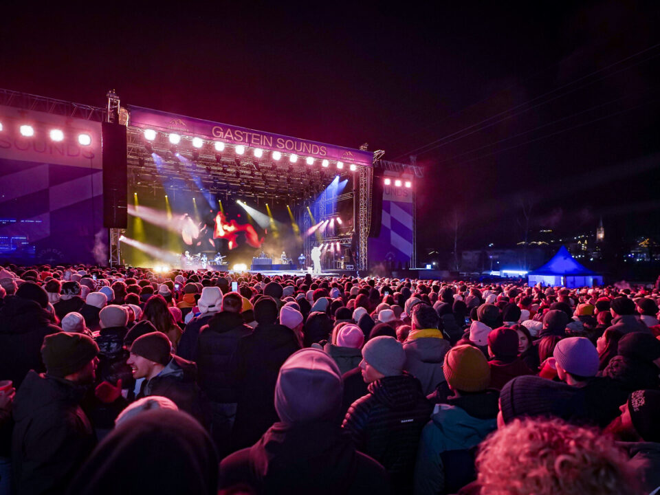 Eine große Menschenmenge verfolgt nachts den Auftritt einer Live-Band auf einer Konzertbühne mit der Aufschrift Gastein Sounds.