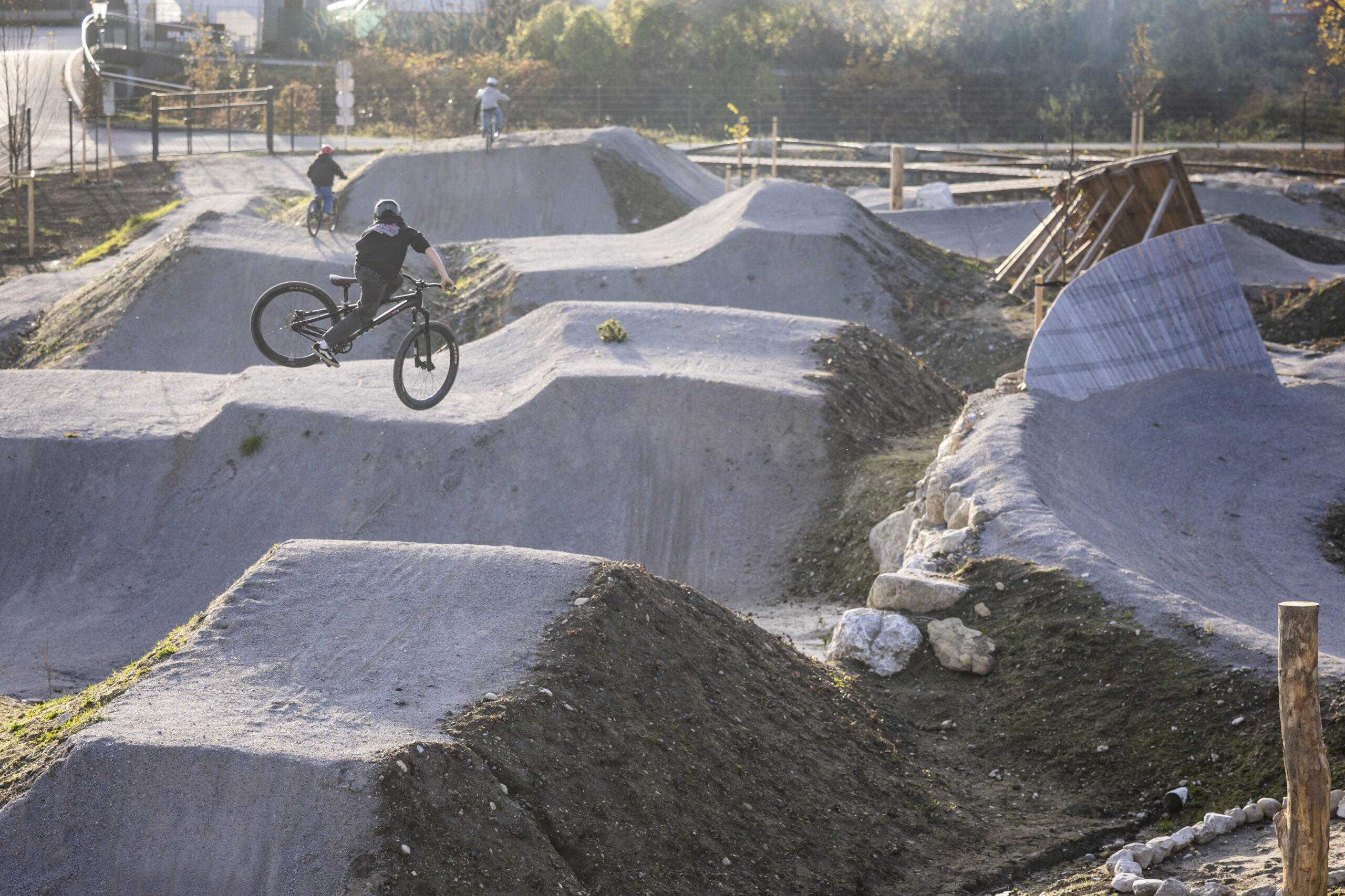 Eine Person vollführt einen Sprung auf einem BMX-Rad in einem Dirt Bike Park mit mehreren Rampen.