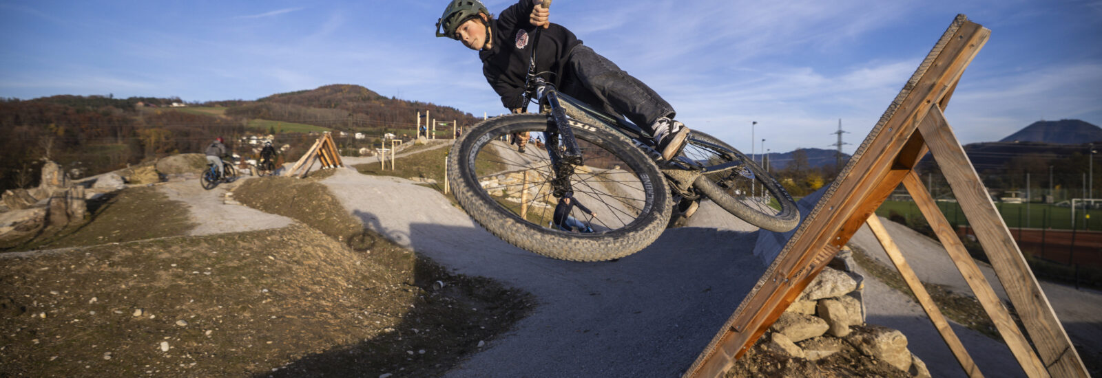 Ein Radfahrer mit Helm fährt mit seinem Mountainbike auf einem unbefestigten Weg, wobei er eine scharfe Kurve auf einer Holzrampe fährt.