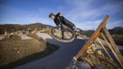 Ein Radfahrer mit Helm fährt mit seinem Mountainbike auf einem unbefestigten Weg, wobei er eine scharfe Kurve auf einer Holzrampe fährt.