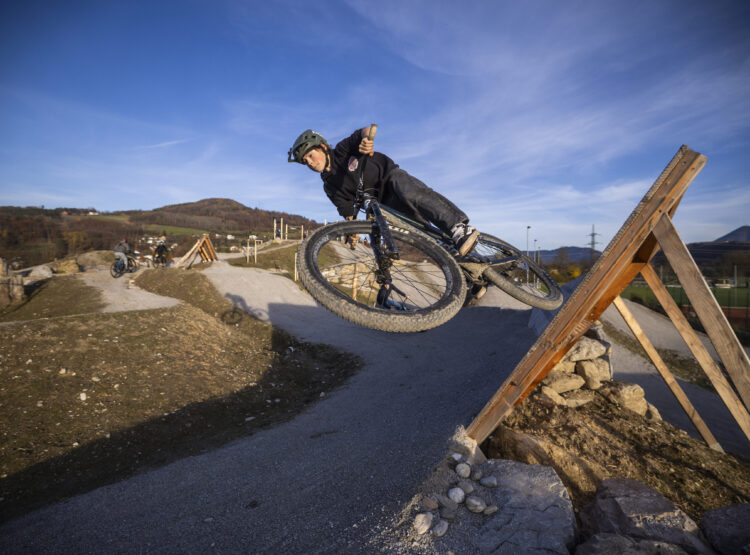 Ein Radfahrer mit Helm fährt mit seinem Mountainbike auf einem unbefestigten Weg, wobei er eine scharfe Kurve auf einer Holzrampe fährt.
