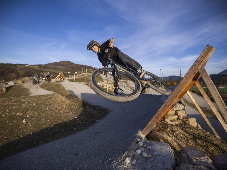 Ein Radfahrer mit Helm fährt mit seinem Mountainbike auf einem unbefestigten Weg, wobei er eine scharfe Kurve auf einer Holzrampe fährt.