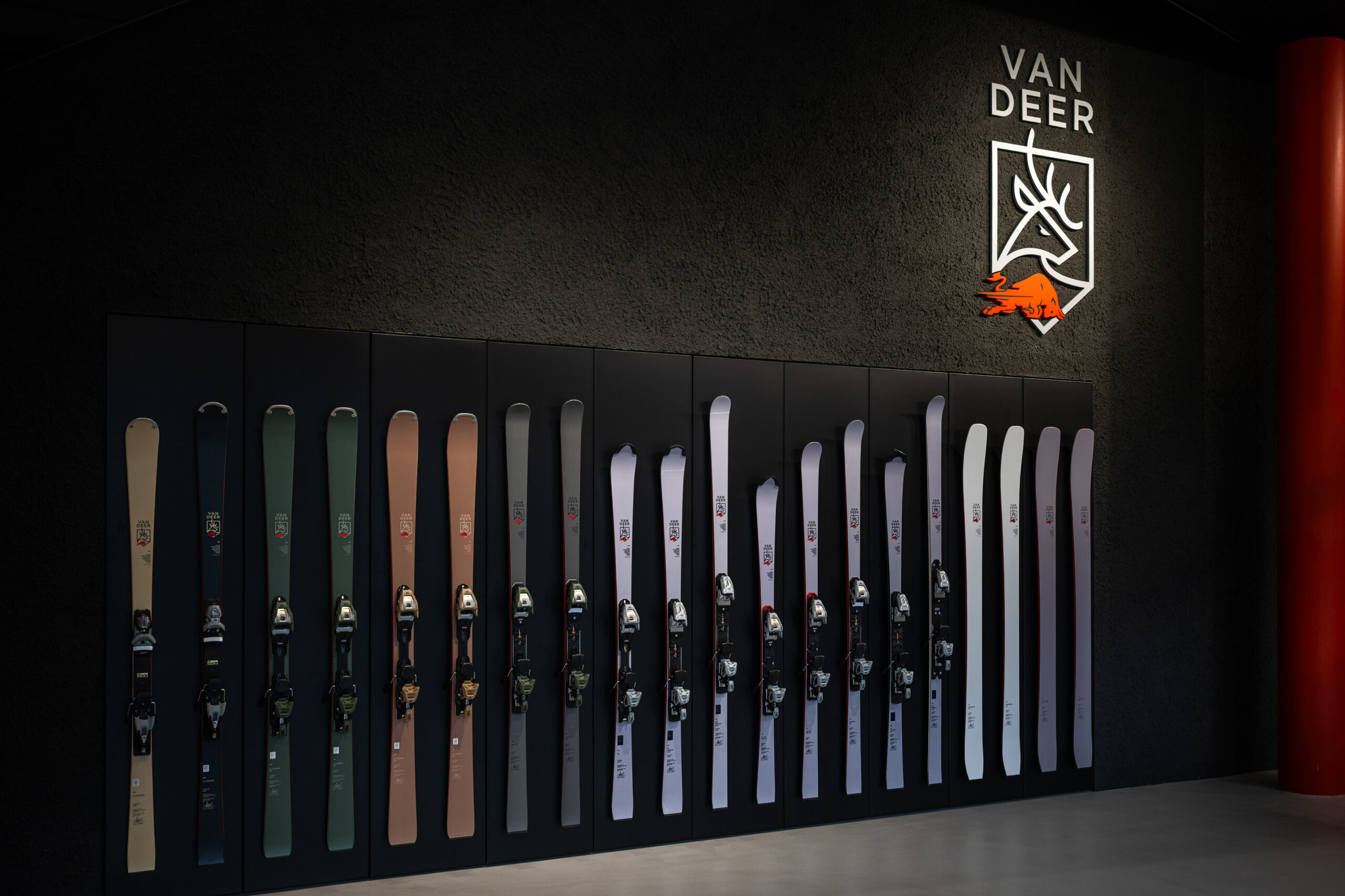 Ein Display mit farbenfrohen Skiern an einer Wand unter dem Van Deer-Logo in einem modernen Ausstellungsraum.