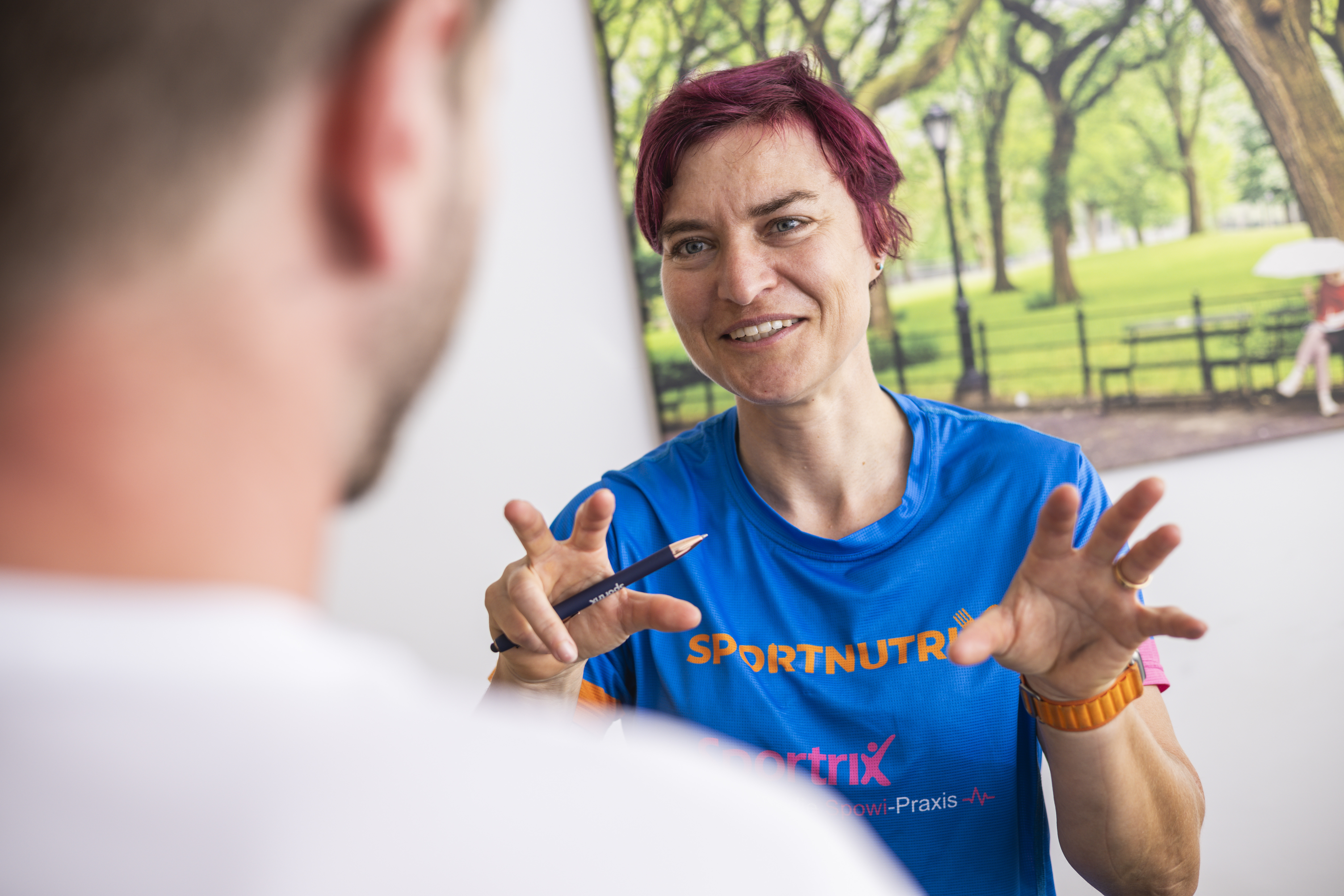 Eine Frau in einem blauen Sporthemd gibt Tipps zum Thema Herzgesundheit und Training, während sie sich in einem Raum unterhält.