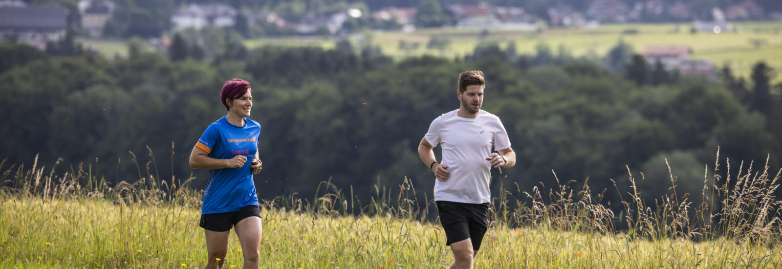 Zwei Menschen joggen durch eine Wiese, entdecken Tipps zum Thema Herzgesundheit und Training.