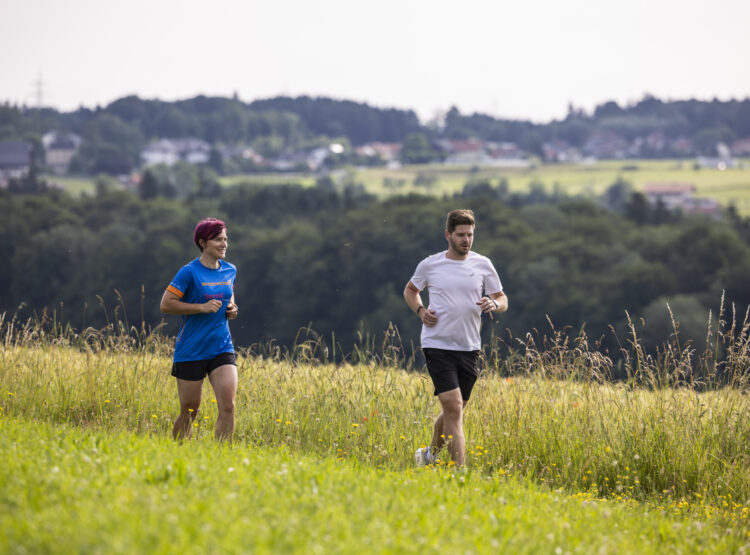 Zwei Menschen joggen durch eine Wiese, entdecken Tipps zum Thema Herzgesundheit und Training.