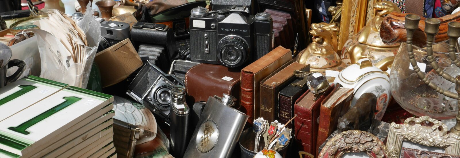 Ein vollgestopfter Tisch mit alten Schätzen von Flohmärkte in Salzburg - Kameras, Bücher, Rahmen und Antiquitäten.