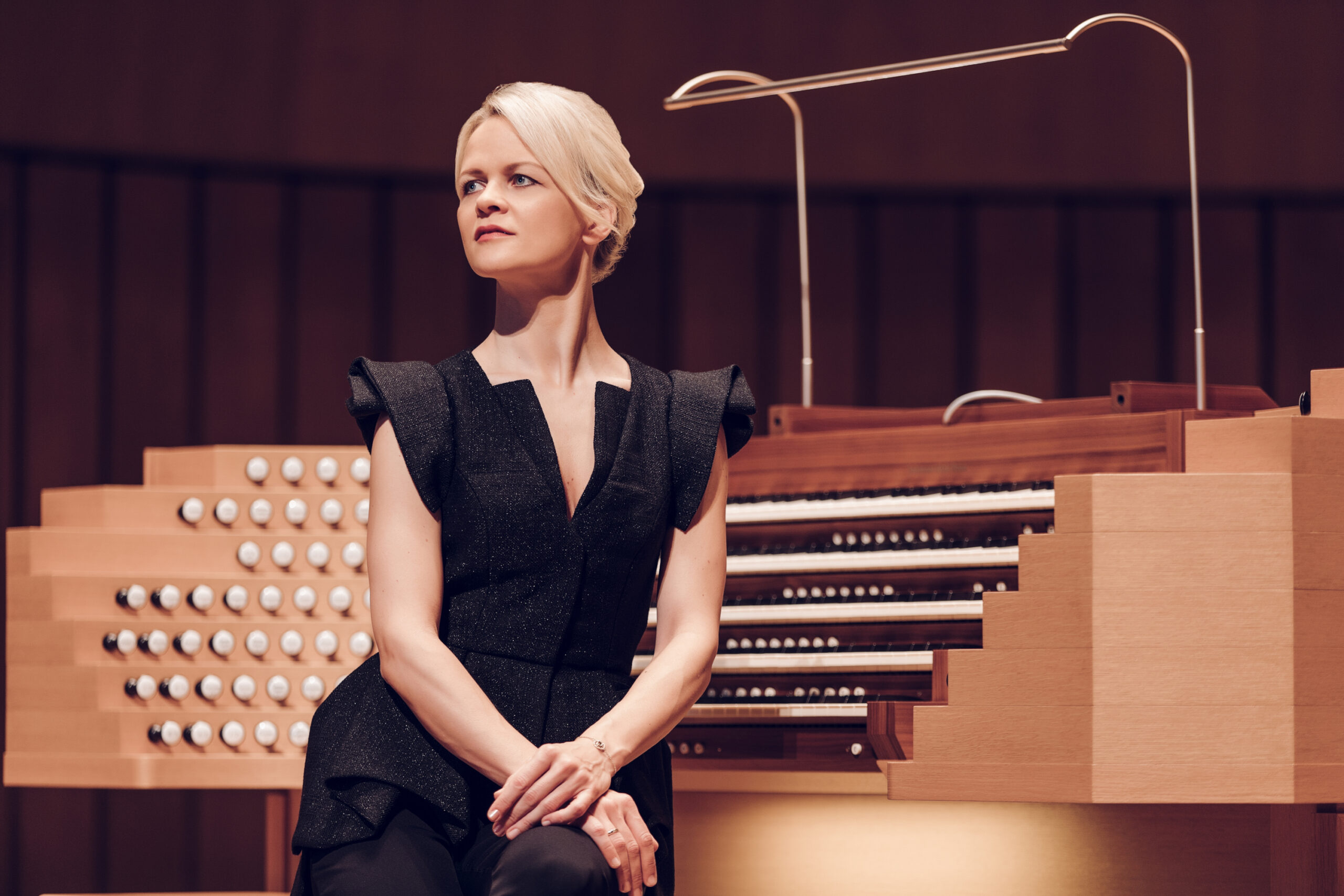 Eine Frau in f&ouml;rmlicher Kleidung sitzt neben einer gro&szlig;en Pfeifenorgel und schaut nachdenklich in die Ferne.