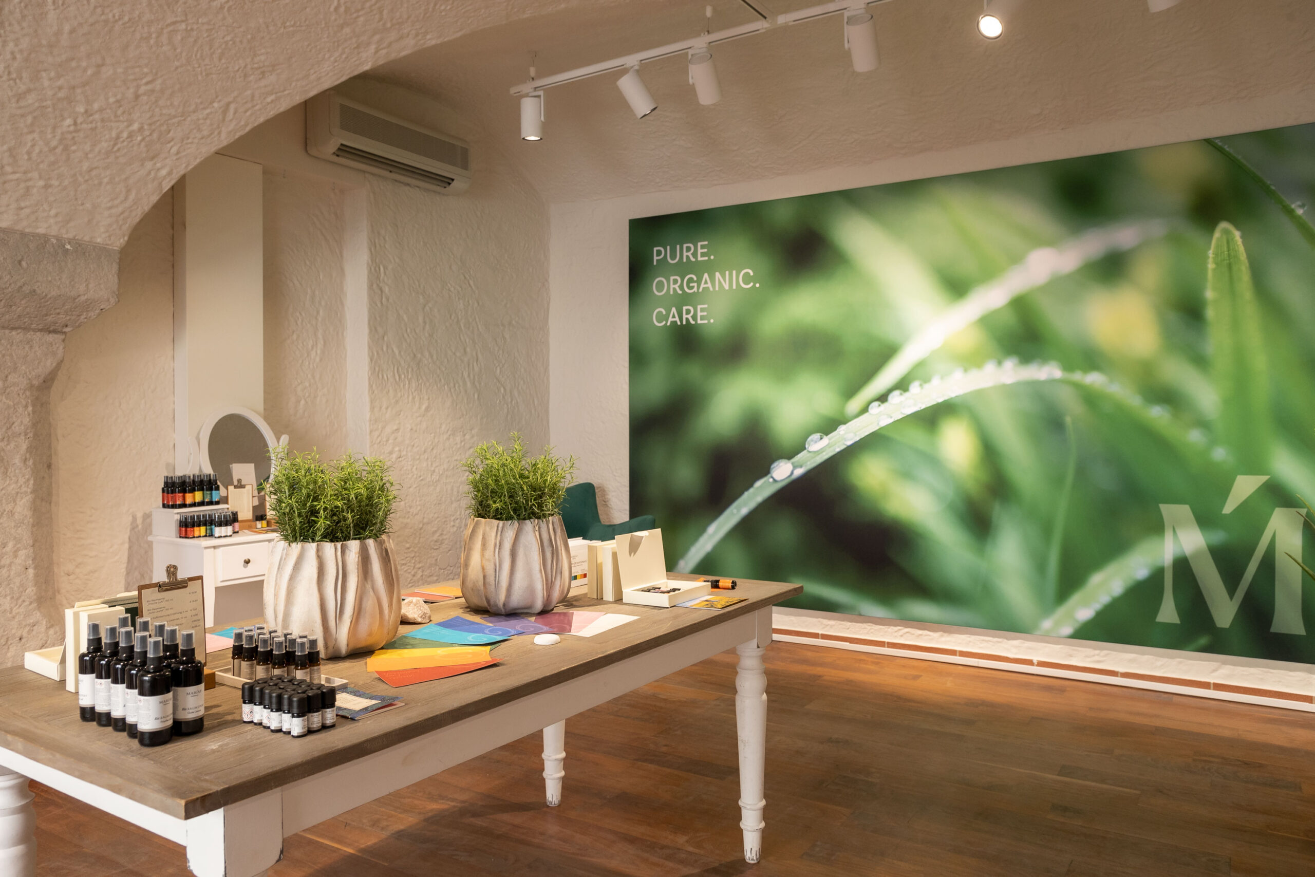 Modernes Geschäft mit einem grünen Naturwandbild, Topfpflanzen und Marias Biokosmetik Kosmetik auf Schautischen.
