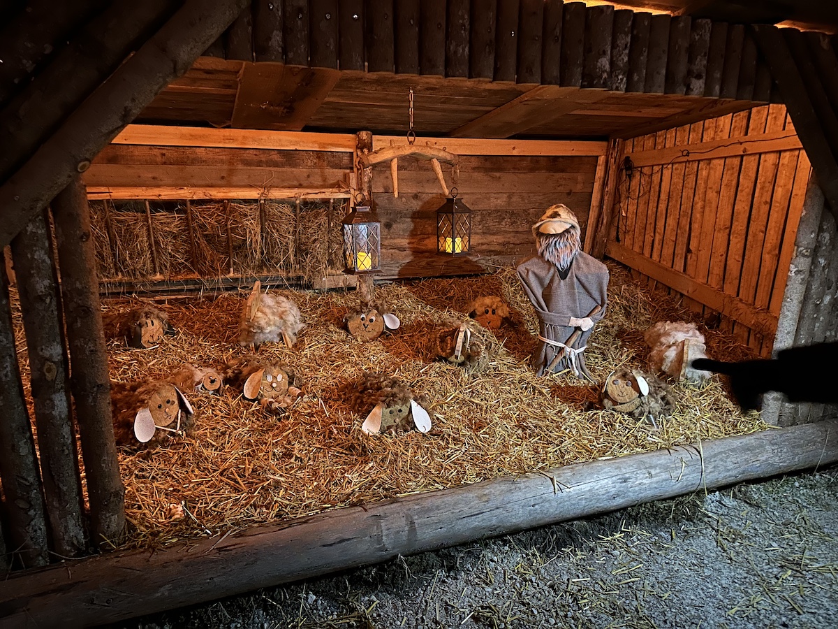 Eine Bramberger Laternenweg-Krippe mit Tierfiguren aus Stroh und Holz in einem Holzstall.
