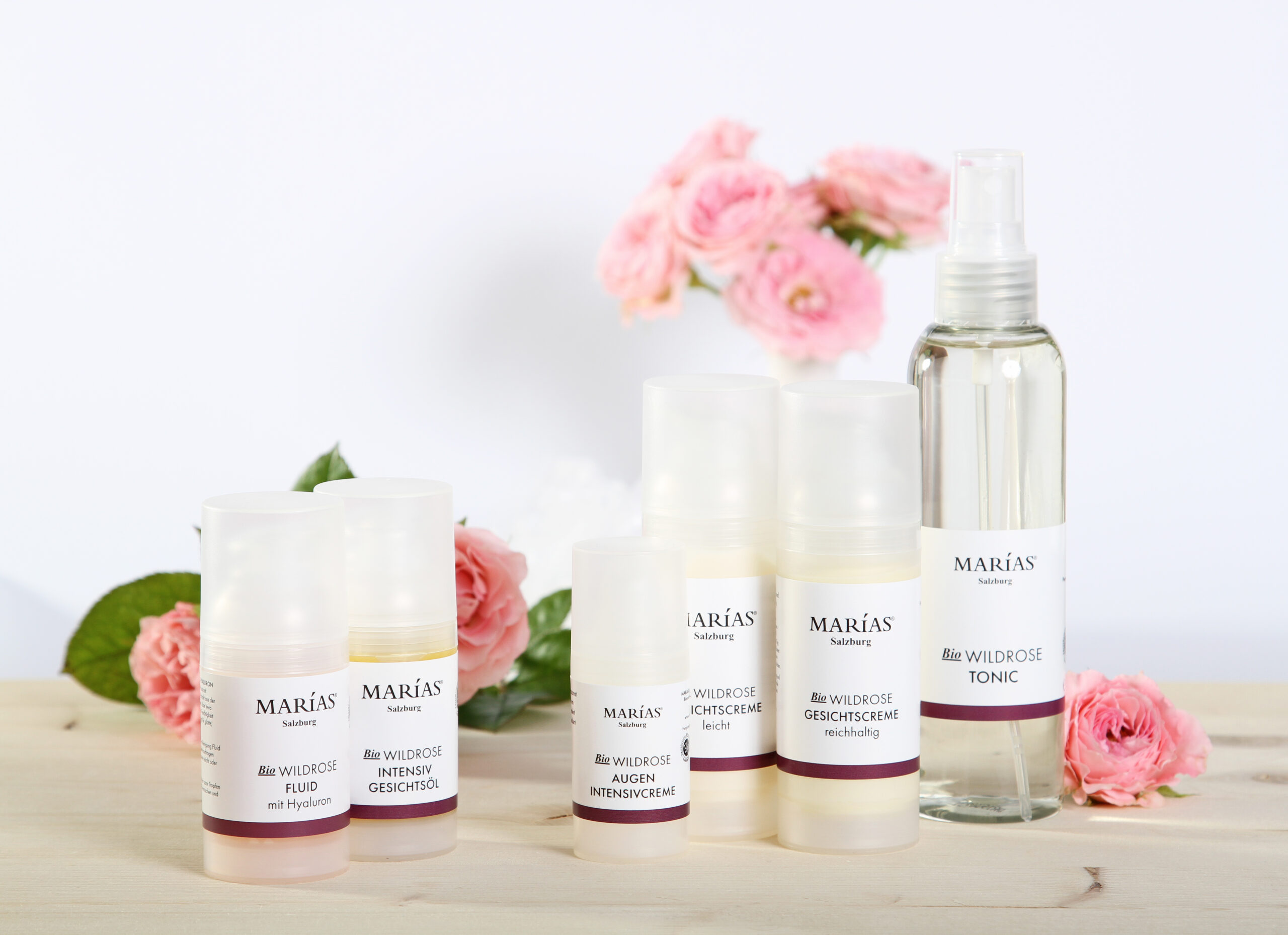 Hautpflegeprodukte von Marias Biokosmetik, einem Salzburger Unternehmen, auf Holz mit rosa Rosen im Hintergrund.