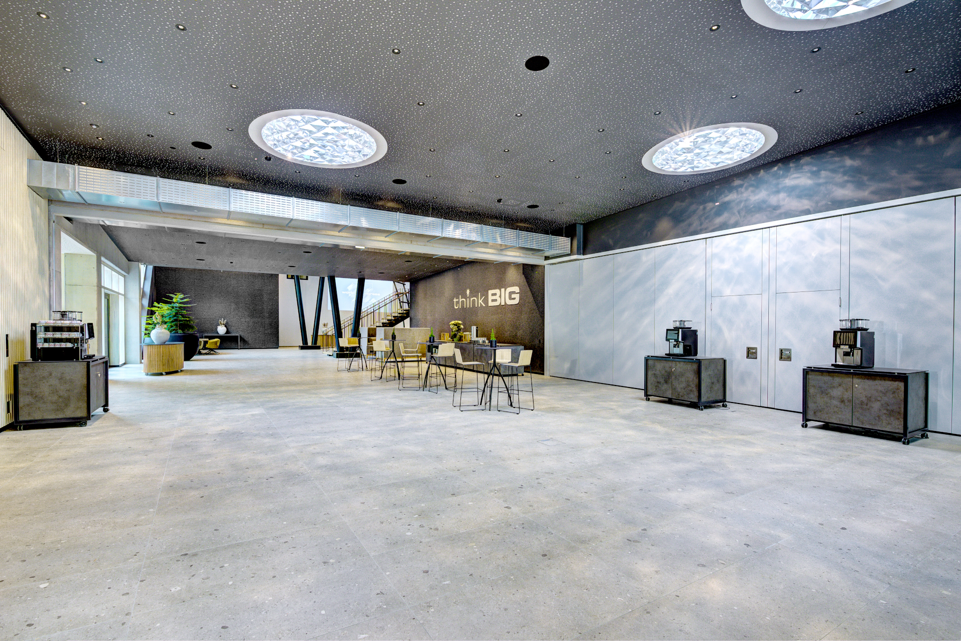 Moderne Lobby im Kongresszentrum mit hohen Decken, Oberlichtern, bequemen Sitzgelegenheiten und dem Hinweis "Think BIG" an der Wand.