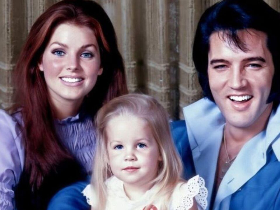 Ein lächelnder Mann und eine lächelnde Frau mit einem jungen Mädchen zwischen ihnen posieren für ein Porträt vor einem Vorhang.