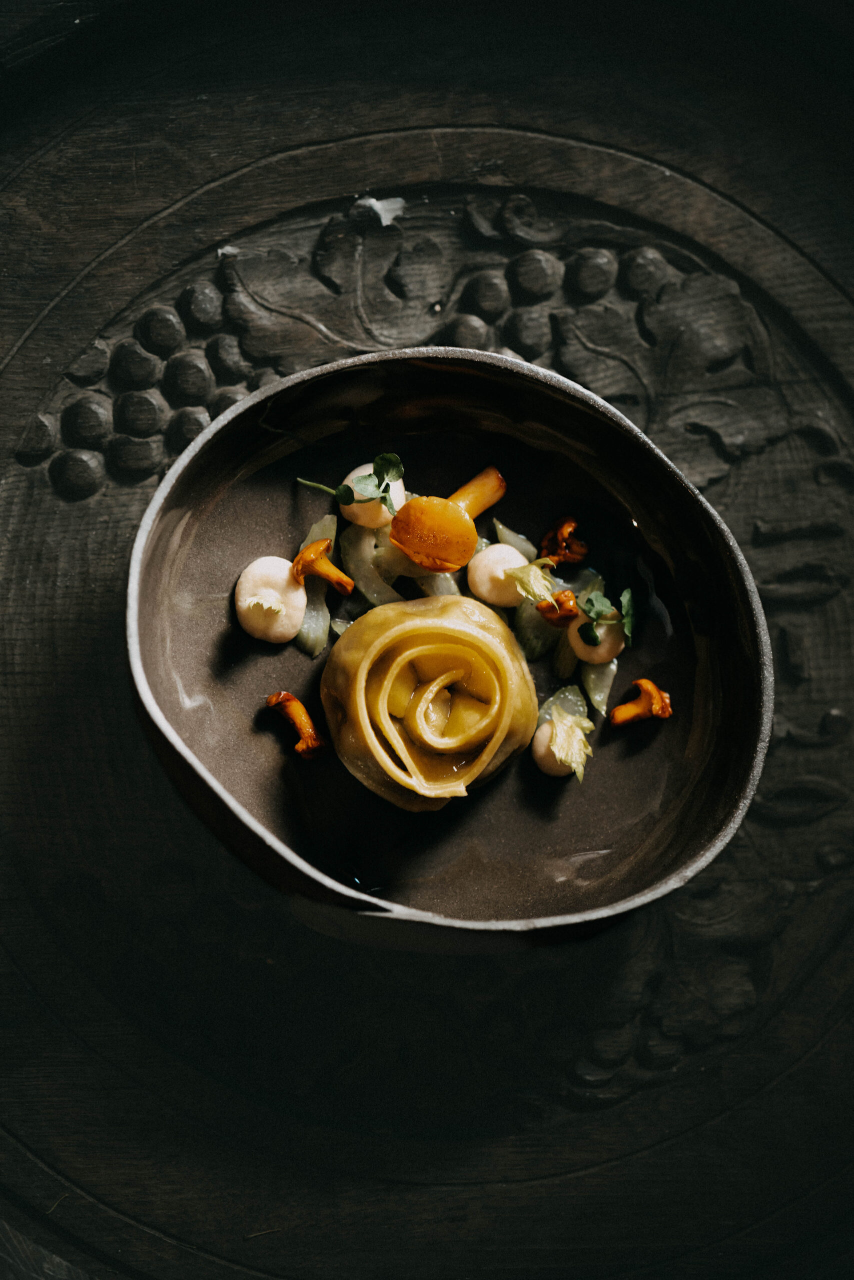 Eine Gourmet-Nudelrose mit Sauce und Beilagen, serviert in einer dunklen, rustikalen Schale auf einem dekorativen Teller.