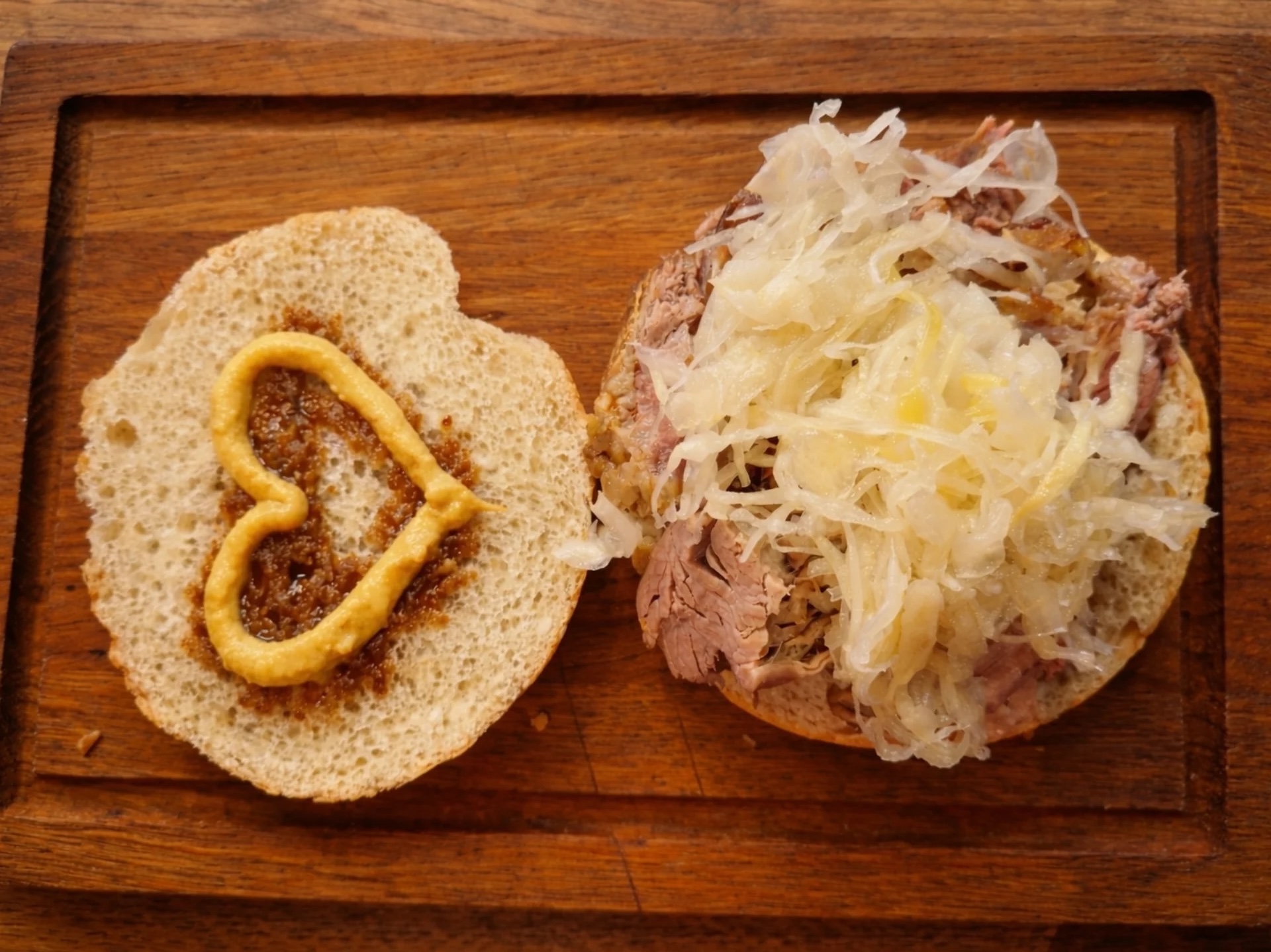 Offenes Sandwich mit Senf in Herzform, Sauerkraut und Fleisch auf einem Holzbrett.