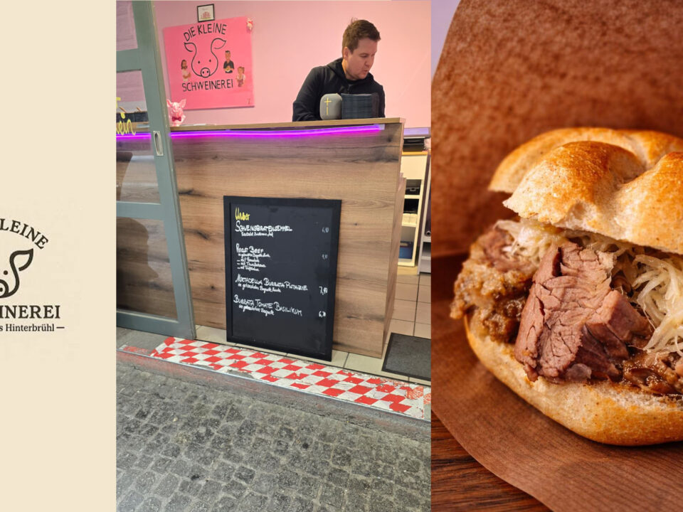 Ein Mann steht hinter einem Tresen, auf dem eine Speisekarte mit Kreide und ein Sandwich mit Fleisch und Sauerkraut abgebildet sind.