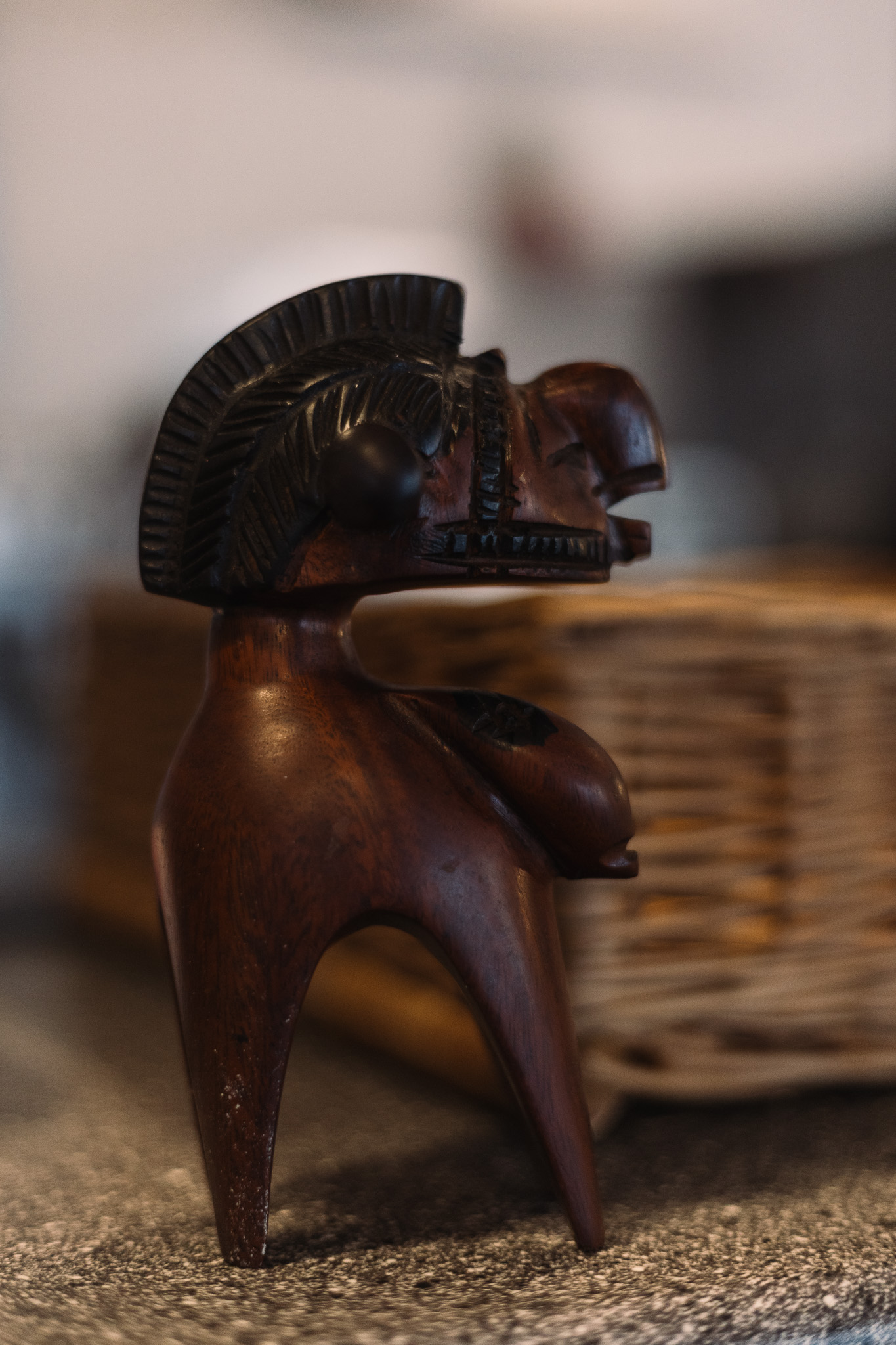 Die geschnitzte Holzfigur "Le Nimba" mit stilisiertem Kopf und Körper steht auf einer strukturierten Oberfläche neben einem geflochtenen Korb.