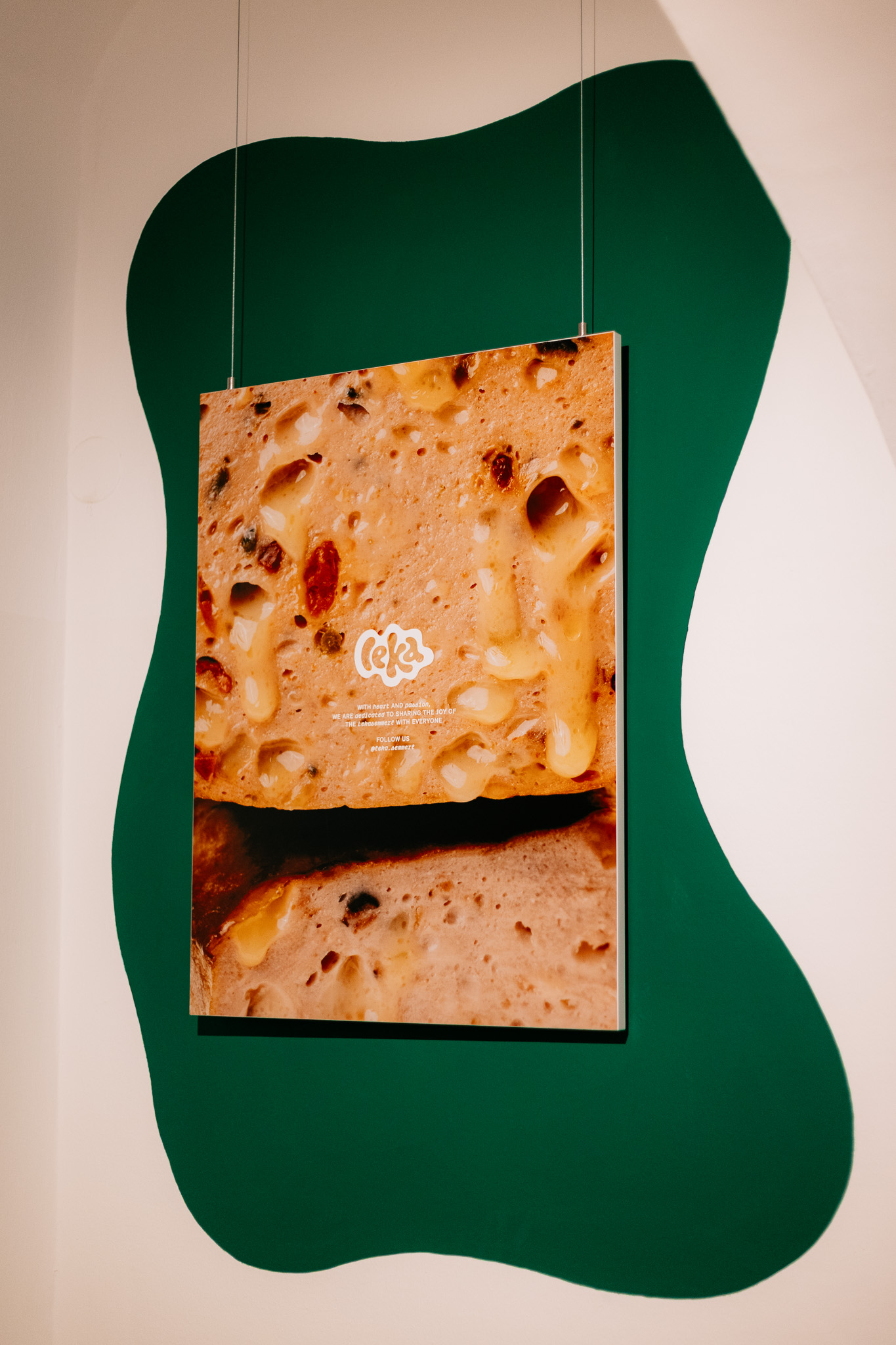 Auf einer Wand ist eine Nahaufnahme von Leberkäse zu sehen, dahinter eine dunkelgrüne abstrakte Form.