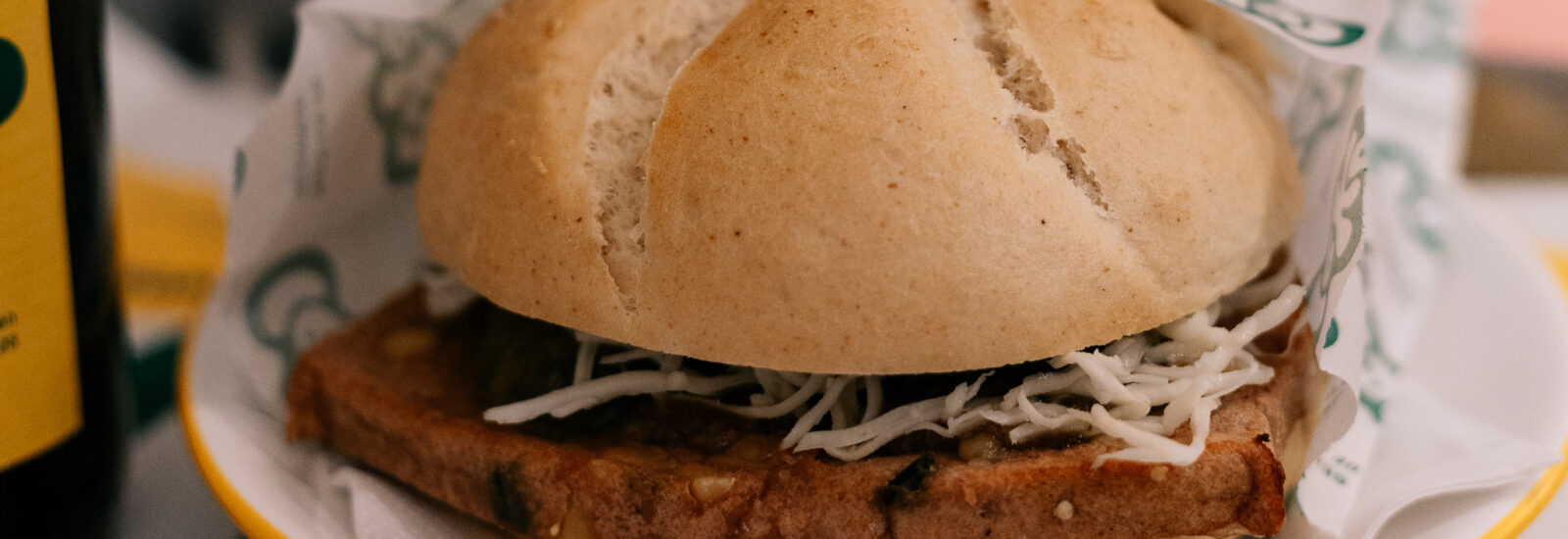 Ein Sandwich mit geriebenem Käse und einer Scheibe Fleisch in einem runden Brötchen auf einem Teller.